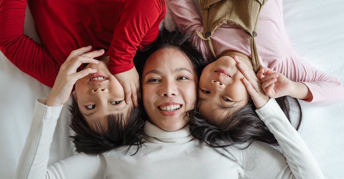 Mother and two children laughing and bonding while lying head to head on the bed at home.