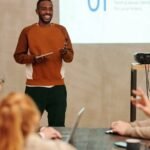 A man delivers a presentation in a modern office to a diverse group of colleagues.