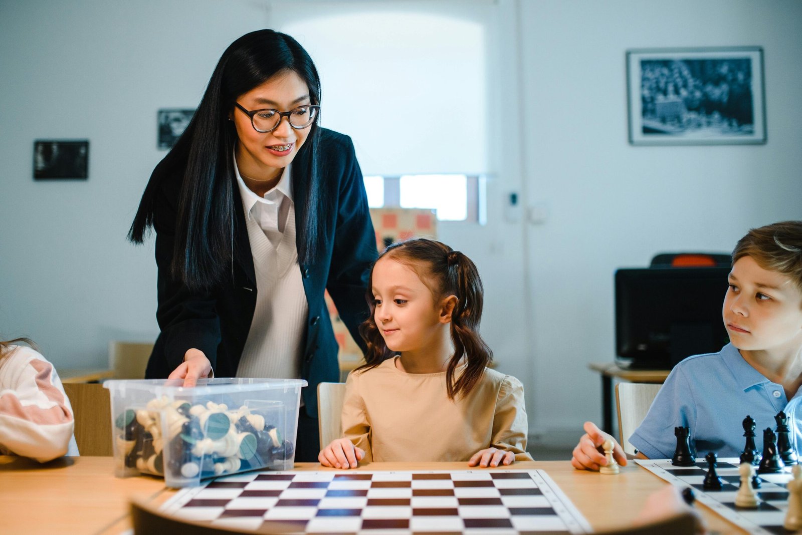 Teacher instructing young students in chess at school, enhancing critical thinking.
