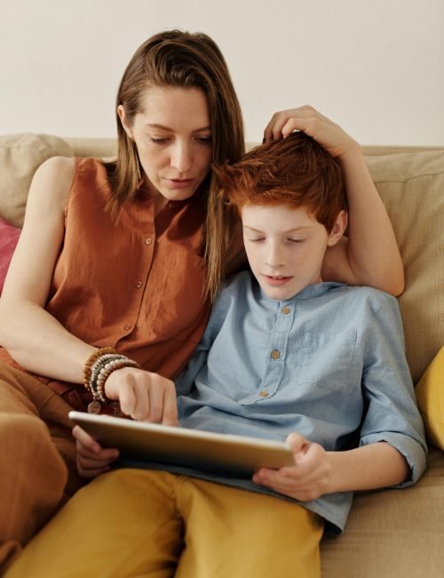 A mother and son bonding as they use a tablet together indoors.